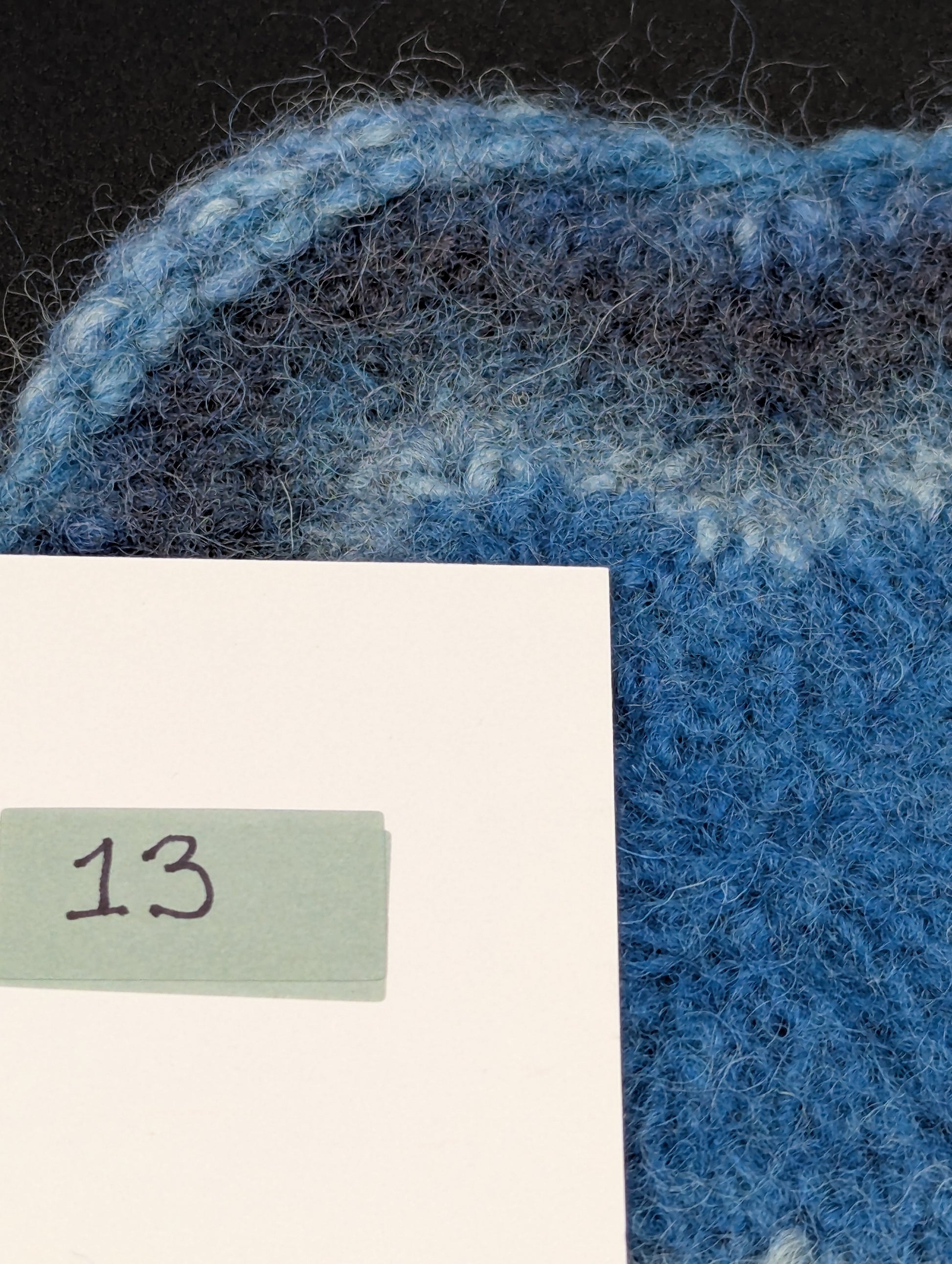Close up of a blue hand knitted and felted coaster. This coaster is number 13.