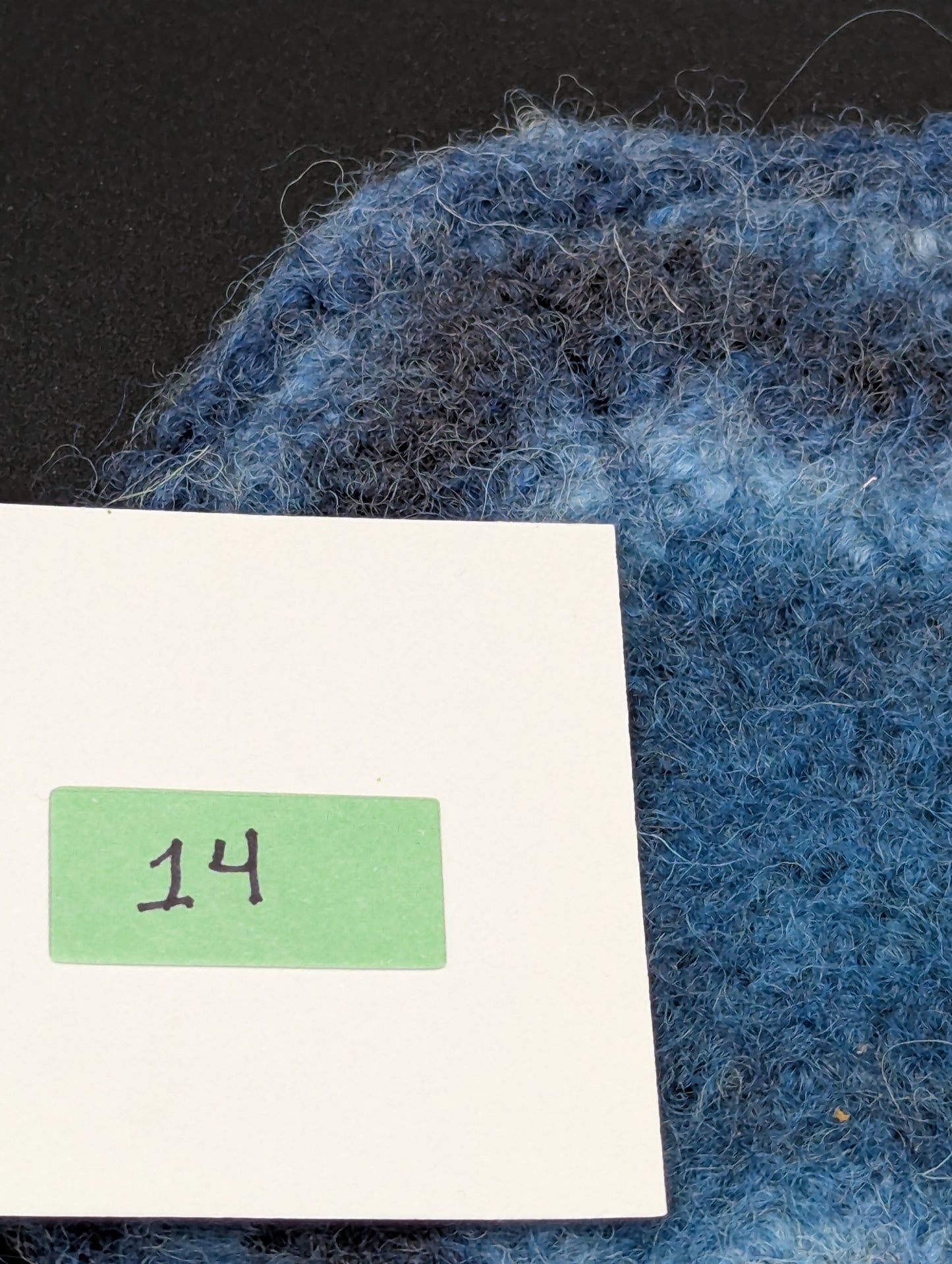 Close up of a blue hand knitted and felted coaster. This coaster is number 14.