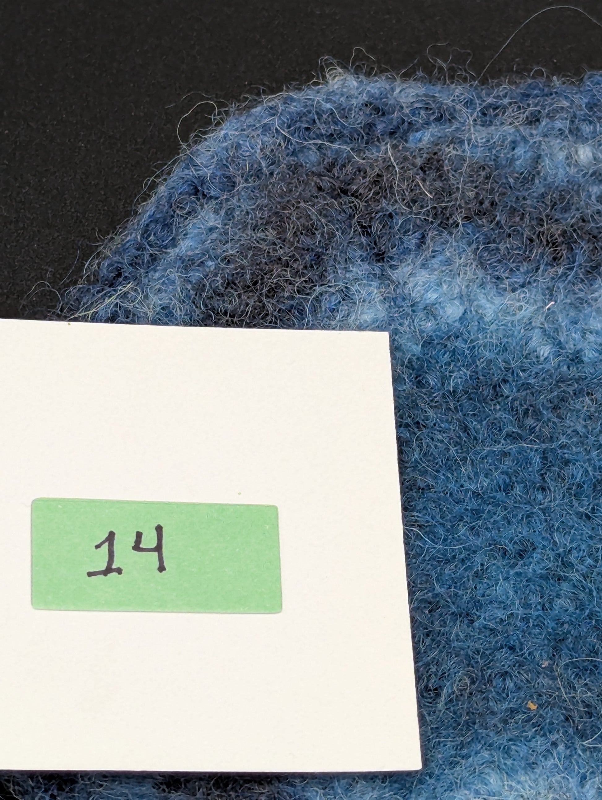Close up of a blue hand knitted and felted coaster. This coaster is number 14.