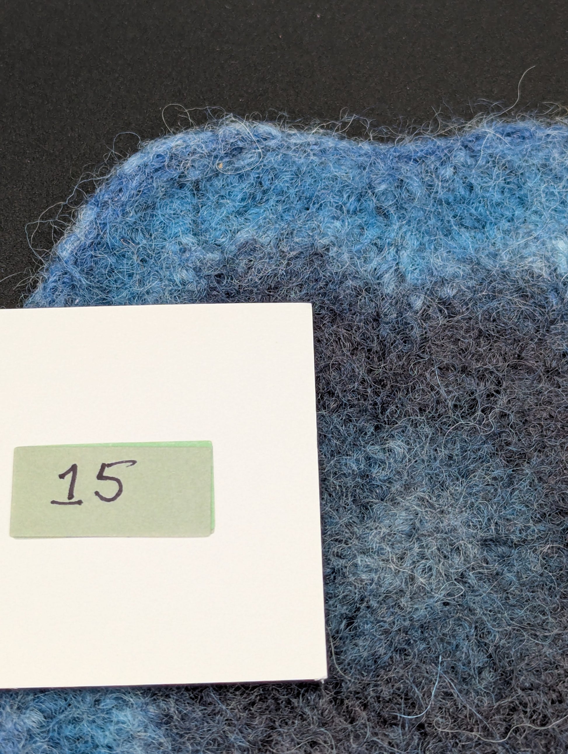 Close up of a blue hand knitted and felted coaster. This coaster is number 15.