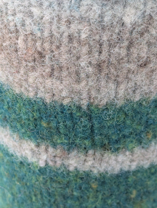 Close-up of a knitted and felted mug cozy in shades of beige, grey, and green