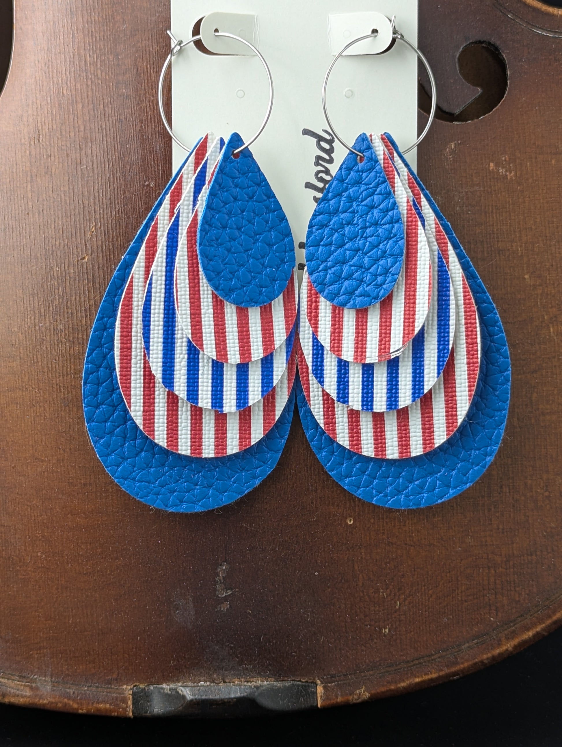 Leather teardrop-shaped earrings with red, white, and blue stripes and solid blue leather on silver hoops. 4 inches in length.
