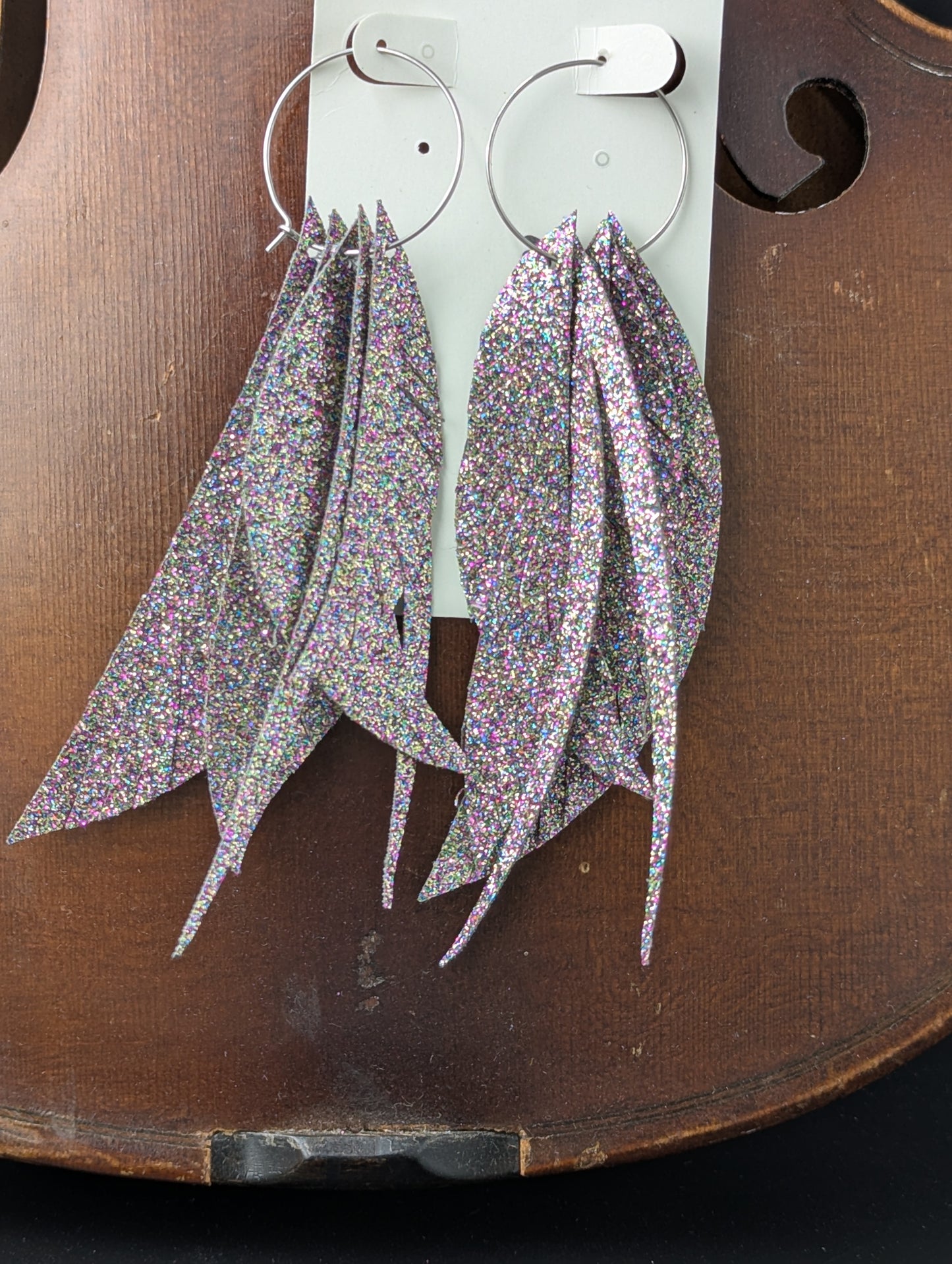 Dark iridescent sparkle feather shaped earrings made from vegan leather on delicate silver hoops. 4.5" in length