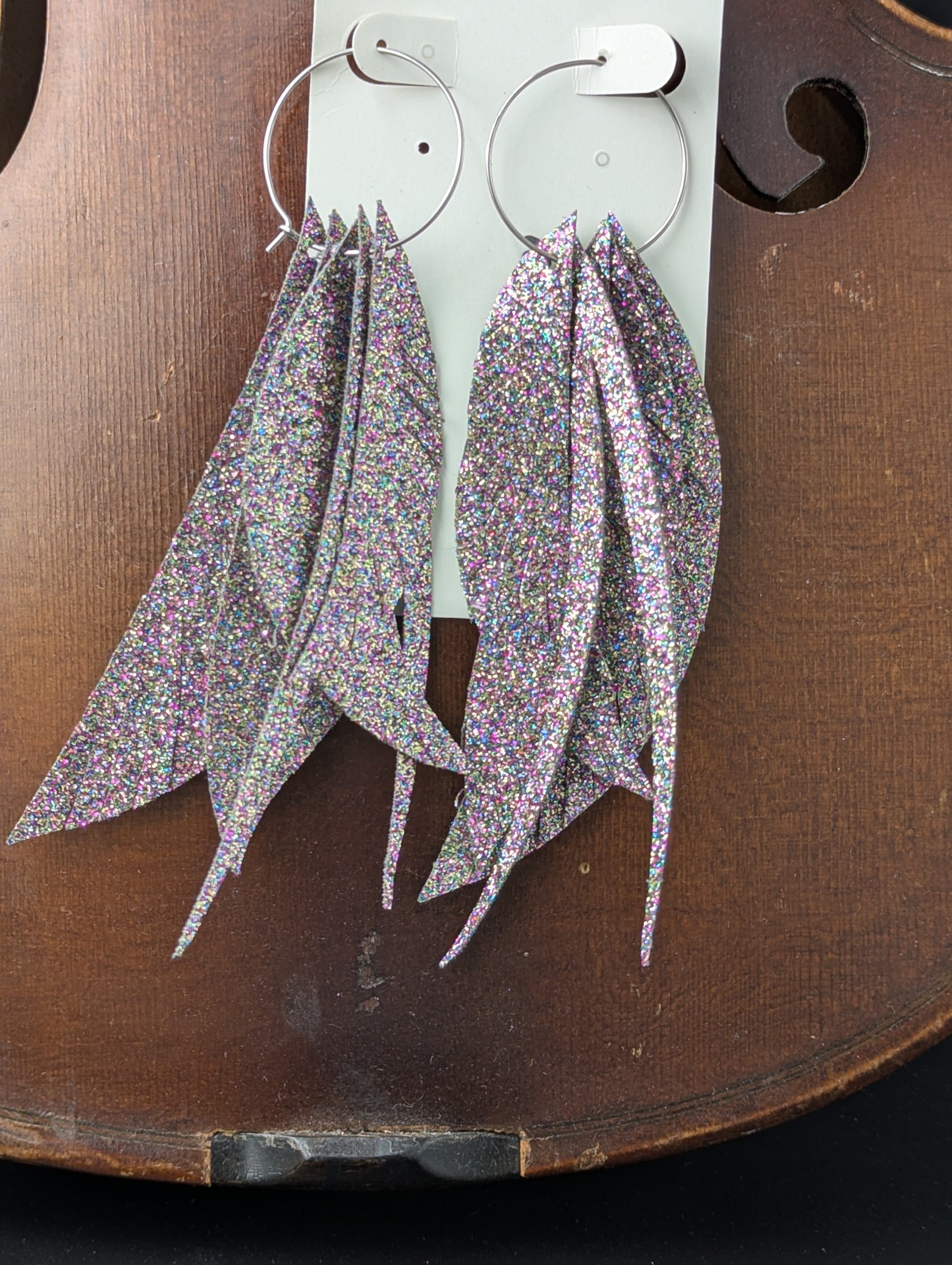 Dark iridescent sparkle feather shaped earrings made from vegan leather on delicate silver hoops. 4.5" in length