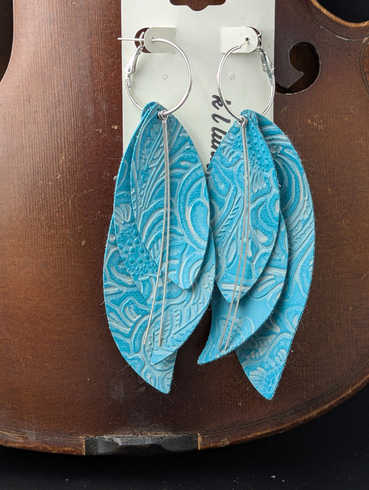 Leather drop shaped earrings with silver accents. Teal with embossed leaves and flowers on silver hoops. 4.5 inches long.