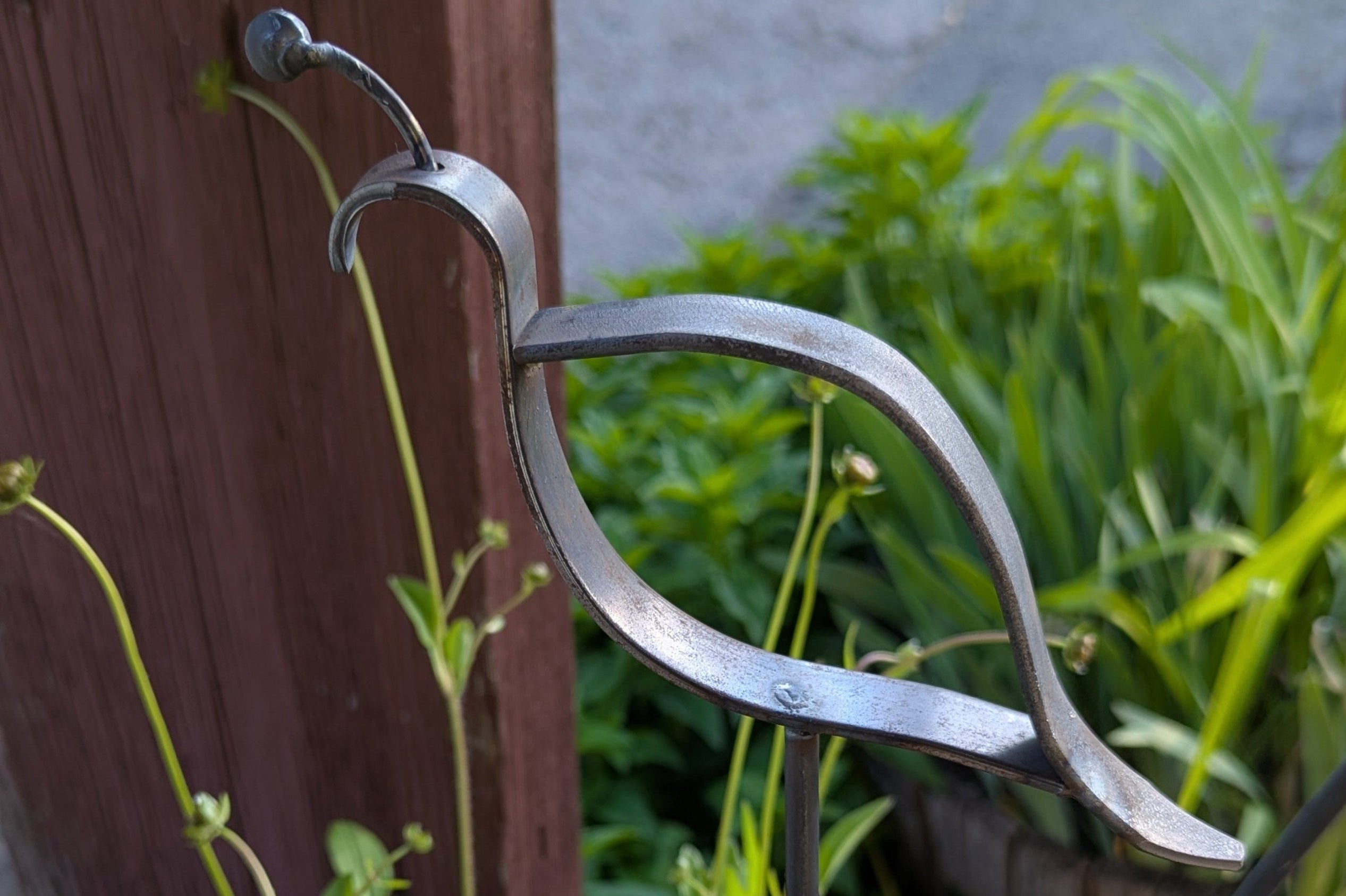Handmade quail metal garden decor with plants in the background