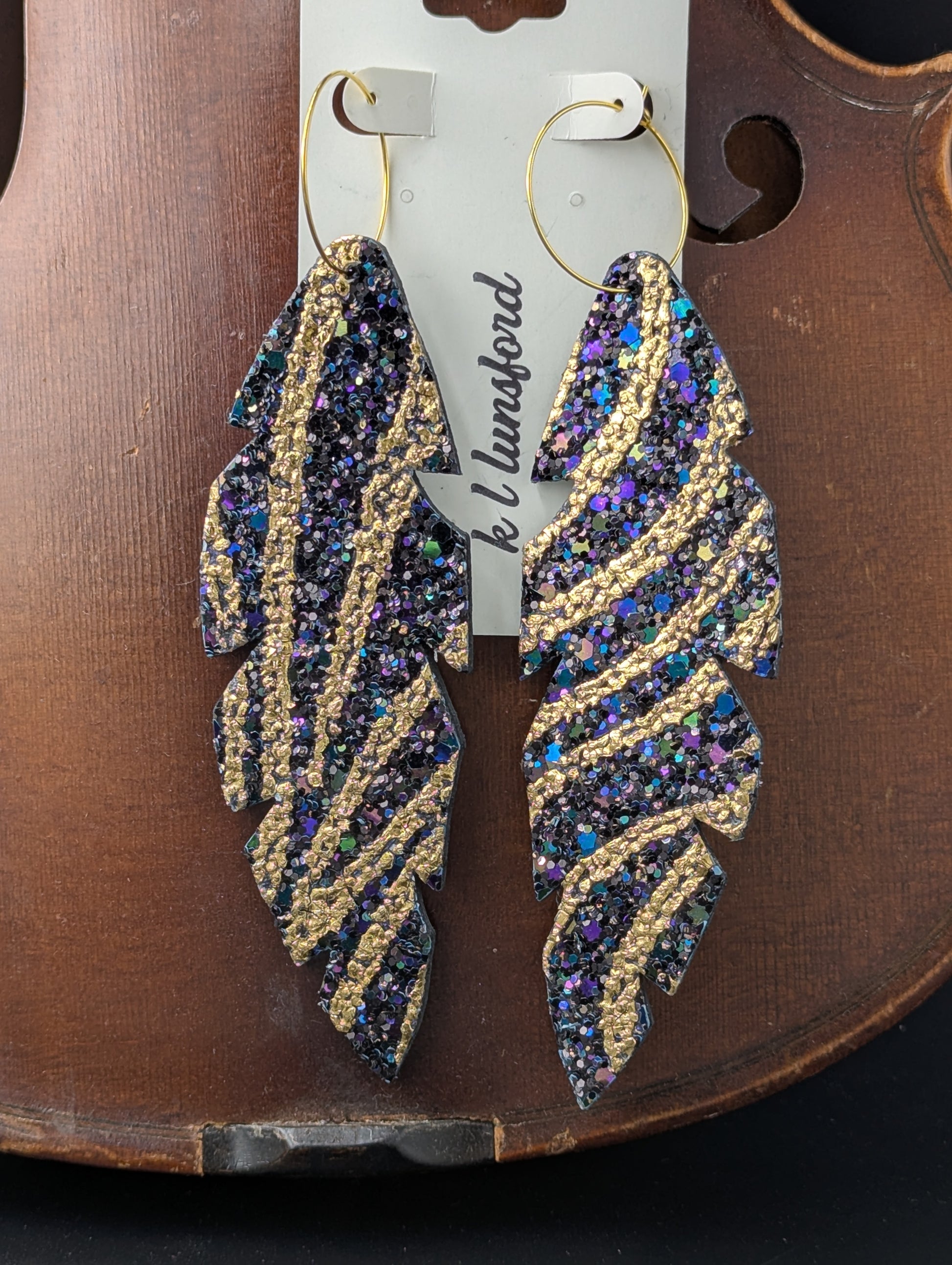 Leather feather shaped earrings with gold hoops. Iridescent black and gold sparkles. 5 inches long